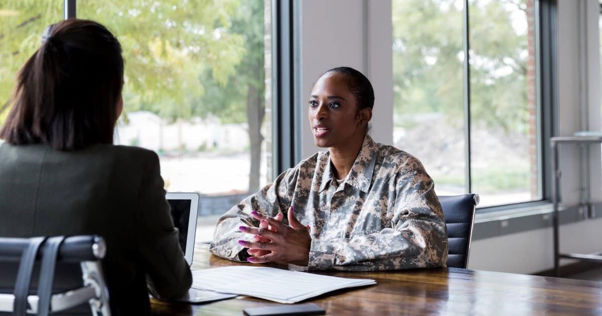 stock photo of a woman engineer in military uniform sitting at a desk and discussing with a civilian coworker